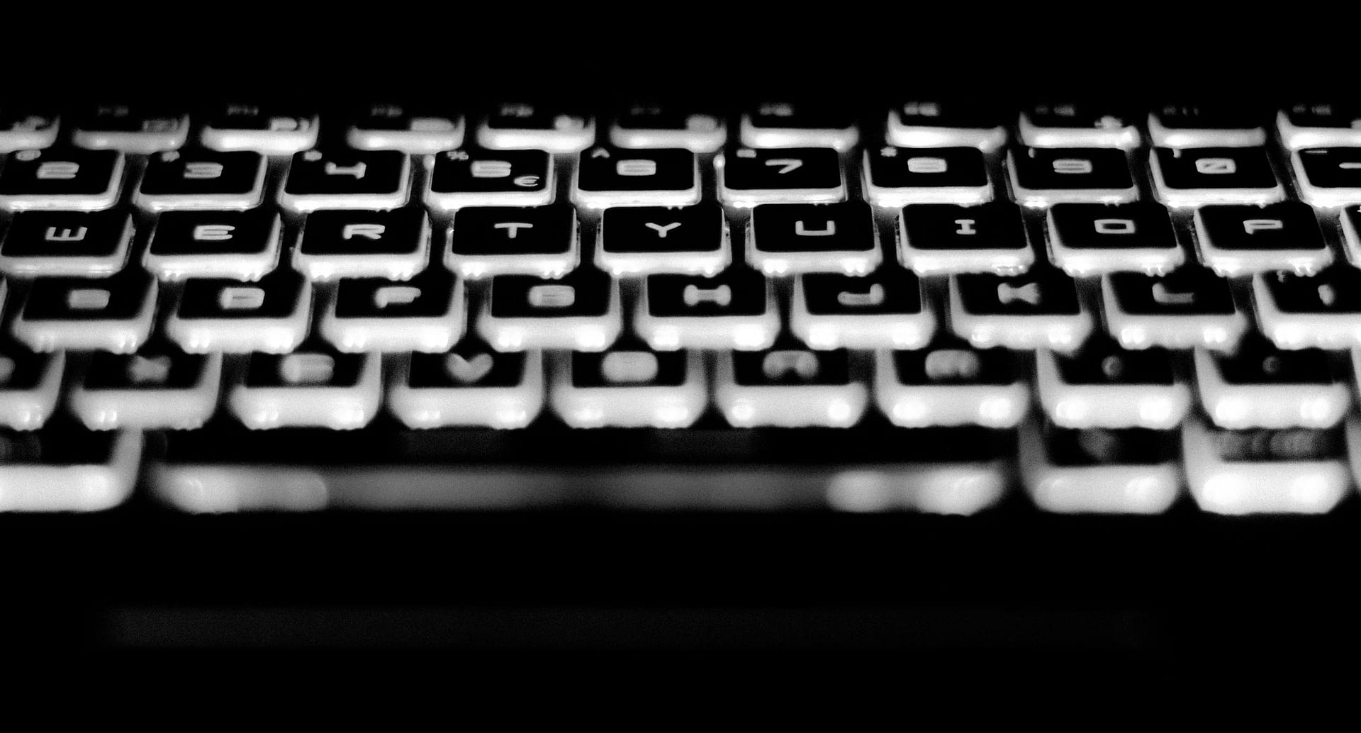 Black and white close-up image of a backlit keyboard showcasing keys and letters. by rocket host