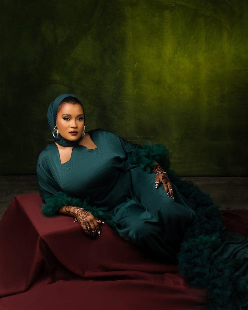 Stylish portrait of a woman in a green dress with henna tattoos against a dark green backdrop.
